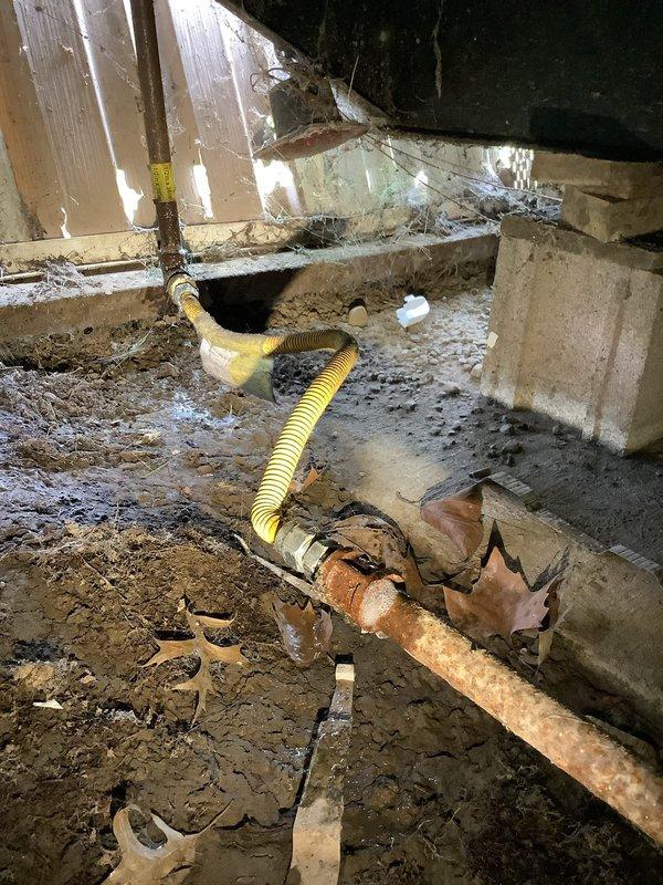 Responded to gas leak investigation following utility company detection of continued leak near meter. Performed pressure test on gas system to isolate leak location, with testing focused on pipes downstream from meter assembly. Inspection revealed severely corroded gas piping in crawlspace with compromised integrity, confirming leak source in piping connected to meter. Pressure gauge reading documented at approximately 5 units, indicating system pressure loss. Corroded metal pipe showing significant deterioration with rust patina throughout surface, connected to flexible yellow gas line. Crawlspace conditions noted with accumulated debris and moisture contributing to accelerated pipe corrosion. Testing confirmed utility company assessment that leak originates from meter-connected piping requiring replacement to restore system integrity and safety.