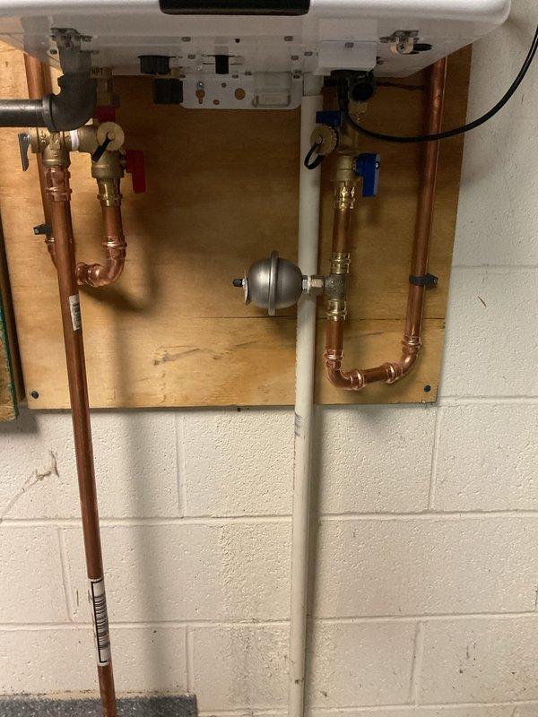 Removed three existing power vent water heaters and replaced them with two new Navien tankless water heating units. Installation included mounting units on wooden backing boards against the wall, connecting copper supply and return lines with brass shut-off valves, installing gray expansion tank with proper piping connections, and running PVC venting. All electrical connections were completed, and the system was tested for proper operation. The installation features organized plumbing with temperature and pressure relief components, ball valves with color-coded handles for easy identification, and Energy Star certified equipment for improved efficiency.