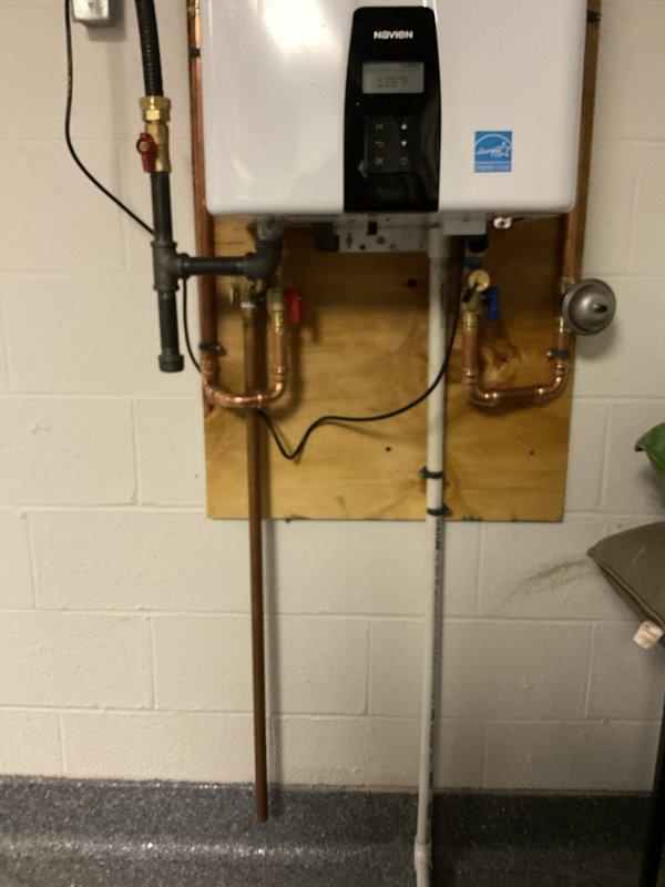 Removed three existing power vent water heaters and replaced them with two new Navien tankless water heating units. Installation included mounting units on wooden backing boards against the wall, connecting copper supply and return lines with brass shut-off valves, installing gray expansion tank with proper piping connections, and running PVC venting. All electrical connections were completed, and the system was tested for proper operation. The installation features organized plumbing with temperature and pressure relief components, ball valves with color-coded handles for easy identification, and Energy Star certified equipment for improved efficiency.