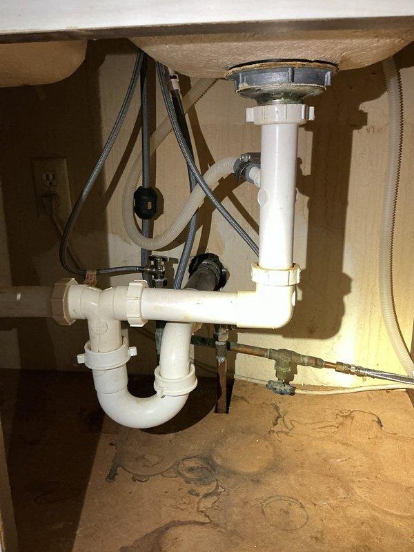 Responded to report of small leak at kitchen sink with water running outside of pipe to basement area. Upon inspection, identified leak in water supply line connection beneath sink. Examined plumbing infrastructure in basement crawl space, including copper water supply lines, vertical drain pipe, and horizontal piping secured with metal hangers. Inspected bathroom sink plumbing assembly featuring PVC drain system with P-trap configuration, flexible braided supply lines, and shut-off valves. Noted previous water staining on cabinet floor indicating past moisture exposure. Tightened connection fittings and secured supply lines to eliminate leak. Verified all connections were properly sealed and tested system for proper drainage and water flow.