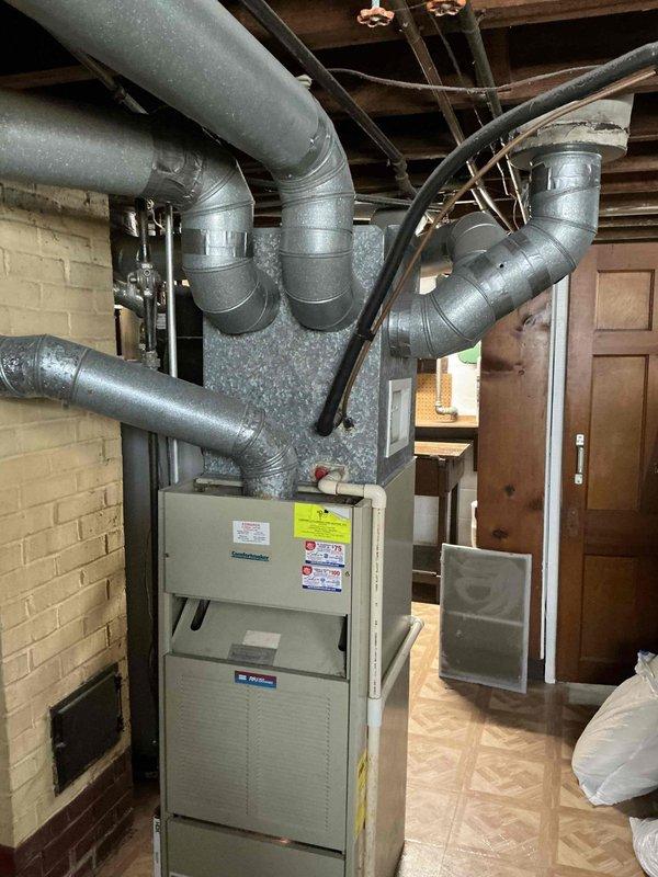 Completed full HVAC system replacement for residential property with 1990-era equipment. Installed new furnace unit in basement mechanical room with updated ductwork connections and electrical components, along with new cylindrical exterior air conditioning unit positioned against brick exterior wall. All systems tested and operational with proper electrical connections, conduit routing, and integration with existing infrastructure.