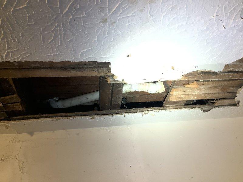 Responded to a service call for a bathtub that was not draining properly. Upon inspection, identified that access to the drain line would require opening the ceiling below the fixture to properly diagnose the issue. Documented the existing water treatment system in the basement area, including dual-tank filtration setup with associated copper and PVC plumbing connections. Examined damaged ceiling section where drywall had been removed, revealing exposed framing and horizontal PVC drain line running through the cavity. Recommended camera inspection of the drain line once additional access is provided. Scheduled follow-up visit to provide repair quote after property owner completes drywall removal for full access to the affected plumbing.