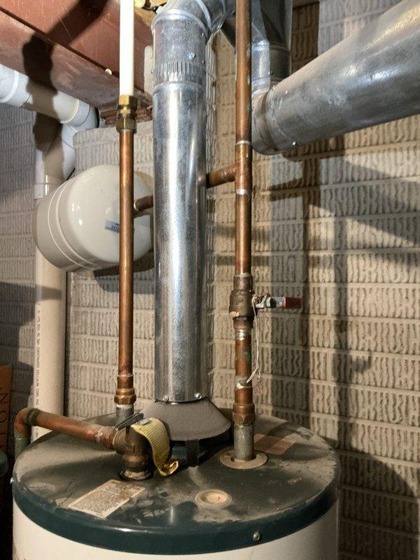 Responded to emergency water heater replacement request for a 10+ year old natural gas unit that had failed with the bottom of the tank compromised. Assessed the existing installation, documented the damaged water heater and surrounding plumbing configuration including copper supply lines, brass valves, expansion tank, and galvanized flue venting system. Provided quote for replacement unit installation with expedited service timeline as requested, including pricing options for Rheem brand equipment to meet customer preferences.