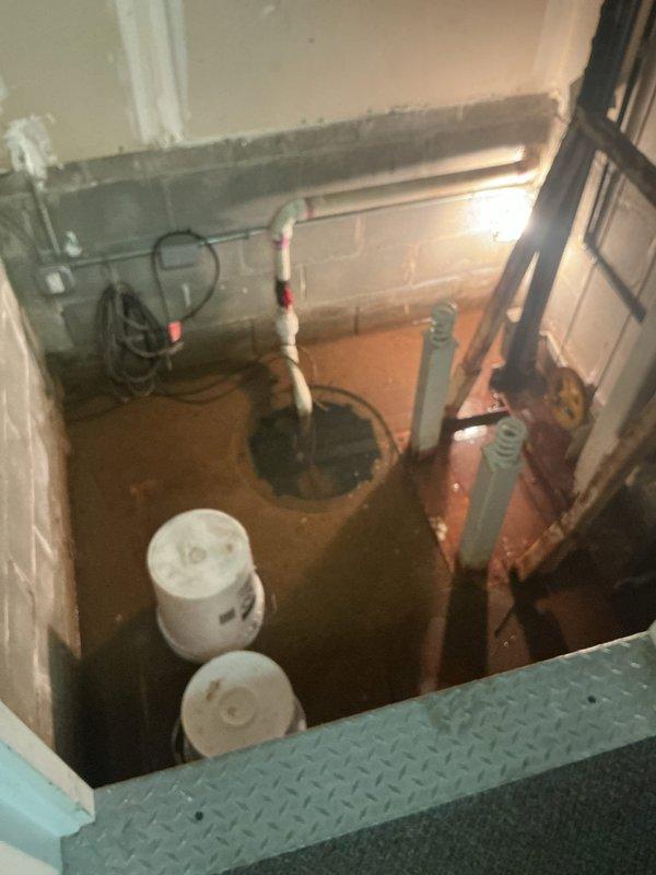 Responded to service call for malfunctioning sump pump located at the base of elevator shaft. Upon arrival, found standing water in the pump basin and surrounding floor area. Inspected sump pump system, including basin, discharge piping, and electrical connections. Identified pump failure preventing proper water removal from the pit. Assessed PVC discharge line routing and verified proper venting. Documented existing water damage and moisture staining on concrete floor surfaces. Photographed pump installation, piping configuration, and overall site conditions for record. Provided recommendations for pump replacement and potential improvements to drainage system to prevent future water accumulation in this utility area.