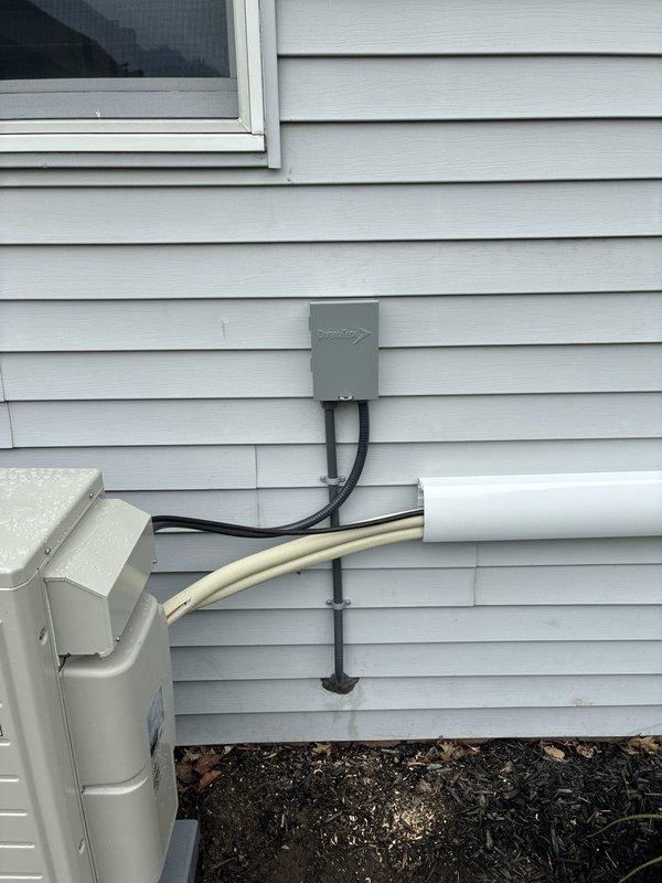 Installed dedicated electrical circuit for mini split system. Ran conduit from new exterior disconnect box mounted on siding to HVAC unit, routing black and tan conduit with proper securing brackets. Extended wiring through basement or utility area, installing gray conduit along ceiling joists and concrete block wall to supply power from main panel to exterior disconnect location.