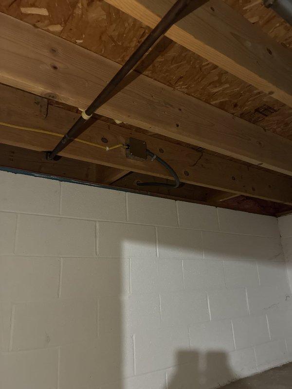Installed dedicated electrical circuit for mini split system. Ran conduit from new exterior disconnect box mounted on siding to HVAC unit, routing black and tan conduit with proper securing brackets. Extended wiring through basement or utility area, installing gray conduit along ceiling joists and concrete block wall to supply power from main panel to exterior disconnect location.