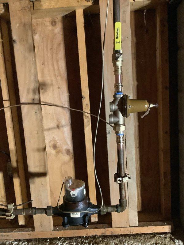 Installed a new pressure reducing valve assembly on the main water supply line in an unfinished interior space. The installation included mounting a Watts pressure regulator with gauge to the exposed wall framing, connecting chrome and brass piping with shut-off valves, and securing all components with appropriate mounting brackets. The pressure gauge was calibrated and the system was tested to ensure proper water pressure regulation throughout the property.