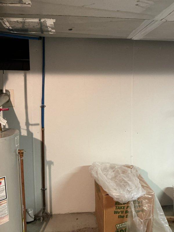 Responded to service call for non-functioning water heater with reported leak from overhead piping. Upon inspection of 50-year-old residential property, identified active water leak originating from supply piping above tanked water heater unit in basement utility area. Ceiling showed evidence of water damage and staining, indicating ongoing moisture intrusion. Assessed copper supply lines connected to water heater, noting red and blue color-coded hot and cold water connections. Repaired leaking pipe connection above water heater to eliminate water intrusion. Verified water heater operation restored to normal function following repair of supply line issue. Confirmed no additional leaks present and system operating properly upon completion.