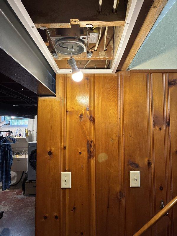 Removed two existing light fixtures controlled by separate switches following kitchen remodel ceiling removal. Installed six 6-inch recessed can lights in wood-paneled ceiling area, with three fixtures per zone, each controlled by its own switch. Junctioned off existing switch legs and ran new wiring to all can light locations. Additionally removed stairway fixture and replaced with matching recessed can light for consistent appearance throughout space. Coordinated installation in two phases: first installed cans and wiring, then returned after ceiling grid and tile installation to complete trim installation with bulbs and baffles to ensure proper fixture placement and avoid interference with ceiling components.