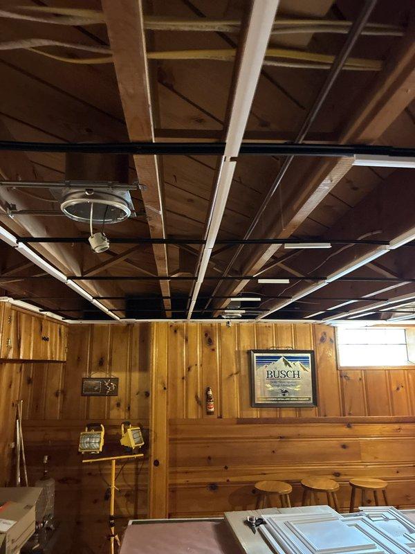 Removed two existing light fixtures controlled by separate switches following kitchen remodel ceiling removal. Installed six 6-inch recessed can lights in wood-paneled ceiling area, with three fixtures per zone, each controlled by its own switch. Junctioned off existing switch legs and ran new wiring to all can light locations. Additionally removed stairway fixture and replaced with matching recessed can light for consistent appearance throughout space. Coordinated installation in two phases: first installed cans and wiring, then returned after ceiling grid and tile installation to complete trim installation with bulbs and baffles to ensure proper fixture placement and avoid interference with ceiling components.