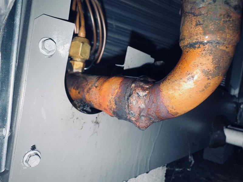Performed leak search on commercial HVAC system and identified severe corrosion on copper refrigerant piping at elbow joint and connection fittings. Documented extensive rust and oxidation damage requiring immediate repair to prevent refrigerant loss and system failure.