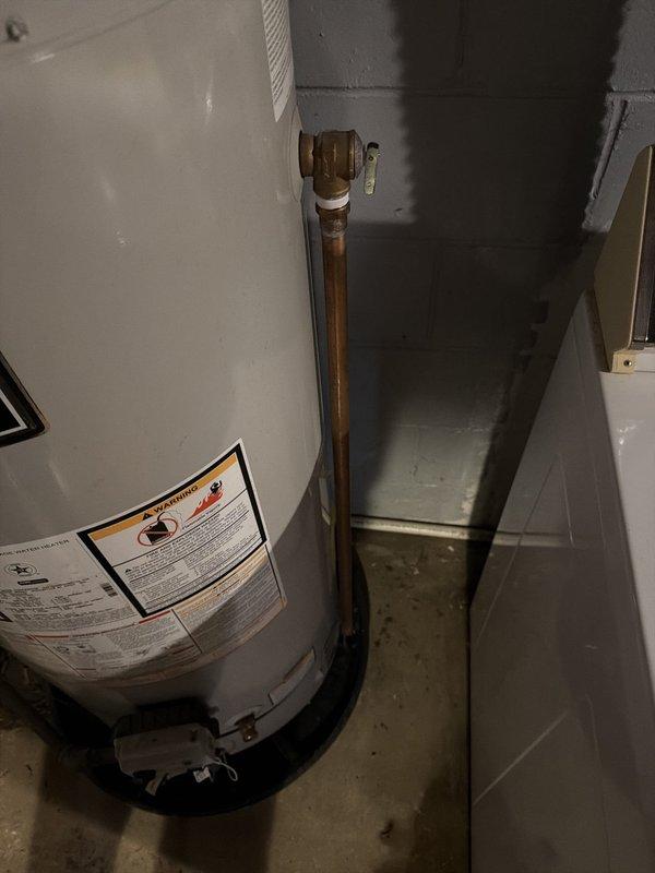 Responded to hot water leak from pipe on right side of water heater causing minor basement flooding in 73-year-old residence. Upon inspection, identified active drip from copper piping connection at top of unit. Tightened compression fitting on outlet pipe to stop leak, verified all connections secure, and inspected surrounding plumbing for additional issues. Confirmed water heater operating properly with no further leakage detected after repair.