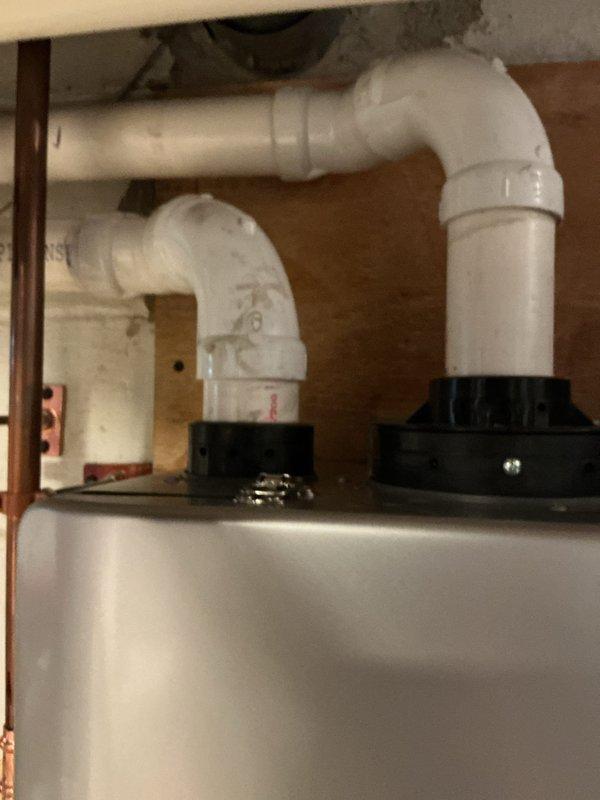 Completed tankless water heater installation in utility room. Installed new copper supply piping with brass ball valve and isolation valves, integrated flow meter with wall-mounted backing board, and connected unit to existing plumbing system. Modified drainage system with new PVC P-trap configuration and rubber coupling adapters to accommodate condensate discharge requirements. All connections tested and verified operational.