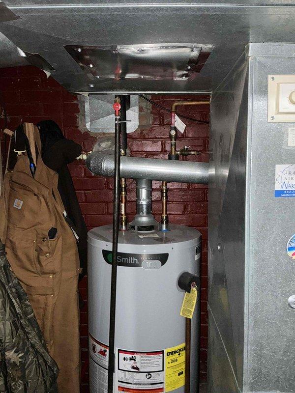 Conducted comprehensive evaluation of 29-year-old HVAC system and provided replacement estimate exceeding $7,000 for complete system upgrade. Documented existing basement air handler installation with metallic finish, black metal plenum, and associated ductwork connections, noting system age and operational status. Photographed mechanical room layout including water heater and electrical components to support replacement proposal specifications.