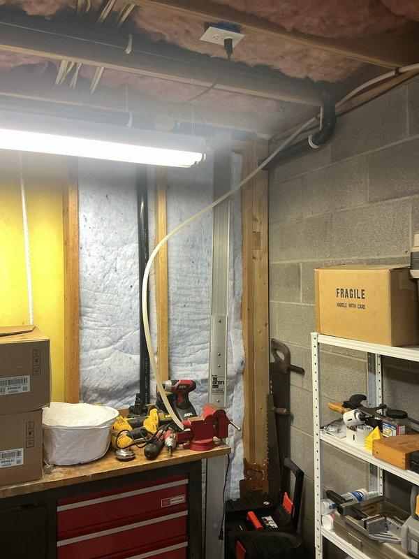 Responded to water leak emergency in utility room with standing water present and empty water softener system. Performed diagnostic inspection of basement plumbing infrastructure, examining exposed piping runs along floor joists and utility room connections. Identified source of water intrusion affecting the water softener supply line. Inspected all visible plumbing connections, supply lines, and drainage systems in the basement workspace area to locate the leak origin and assess extent of water damage to surrounding areas.
