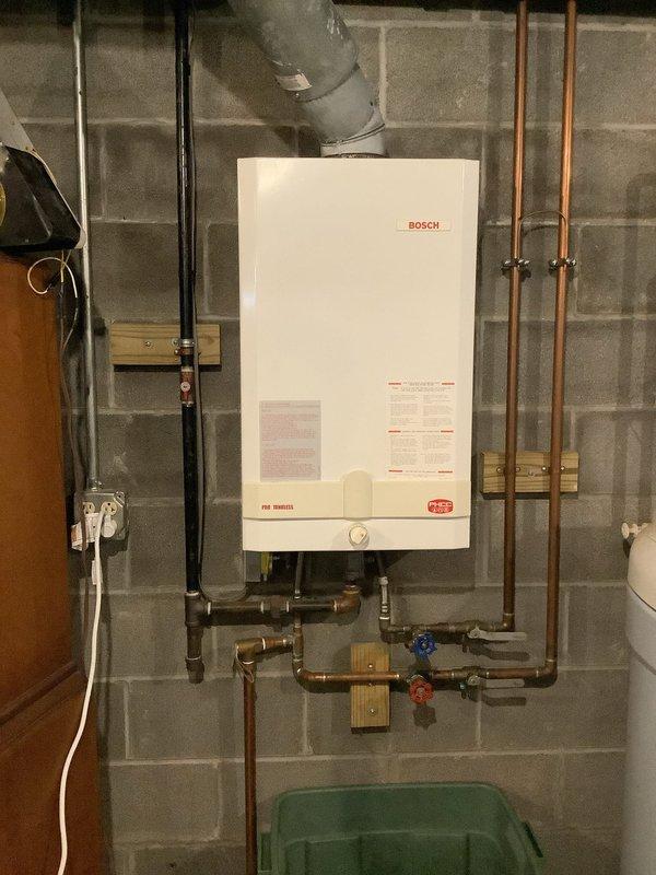 Conducted free estimate for tankless water heater replacement due to loss of hot water supply to upper level fixtures while lower level maintained functionality. Inspected existing Bosch tankless unit mounted on basement wall with copper supply lines, shut-off valves, and PVC venting system. Documented current installation configuration including plumbing connections, gas lines, and electrical supply for replacement planning and customer proposal.