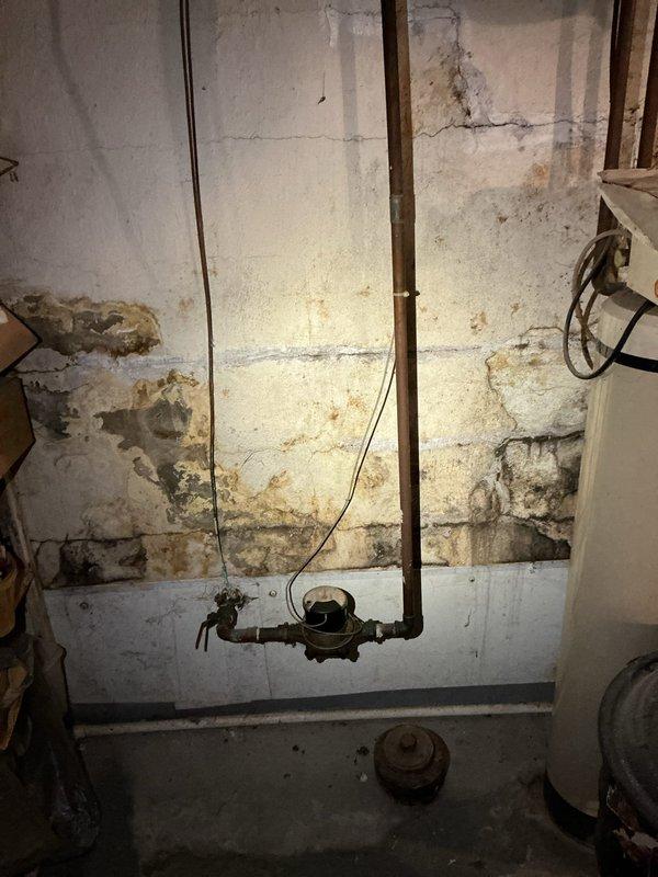 Responded to emergency call for mainline backup in basement. Upon arrival, located heavily corroded main drain cleanout with significant rust deterioration around the access point. Performed cleanout of mainline to restore proper drainage and eliminate backup condition. Noted extensive water damage, efflorescence, and mineral deposits on surrounding basement walls indicating history of drainage issues. Cleanout successfully cleared obstruction and restored flow through main sewer line.