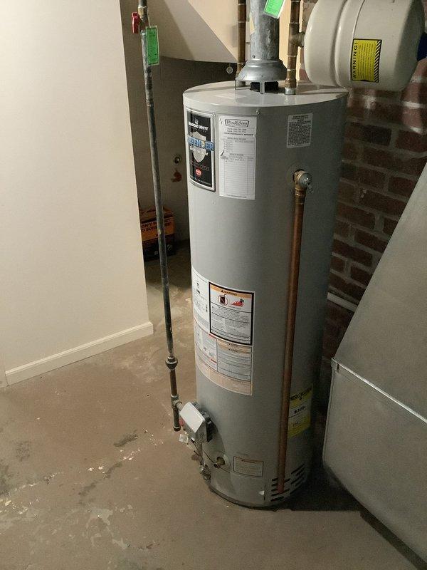 Responded to service call for 13-year-old residential water heater reported to be leaking. Upon arrival, inspected existing tanked water heater unit and confirmed active leak at base of tank, indicating internal tank failure typical of units in this age range. Documented existing installation configuration including copper supply line connections, pressure relief valve placement, and seismic restraint strapping. Customer requested replacement with new unit of comparable capacity, estimated at 40-gallon size based on household needs and existing installation footprint. Photographed existing water heater showing manufacturer labels, energy guide information, plumbing connections, and surrounding mechanical room conditions including brick wall proximity and concrete floor installation area for accurate replacement specifications and permitting requirements.