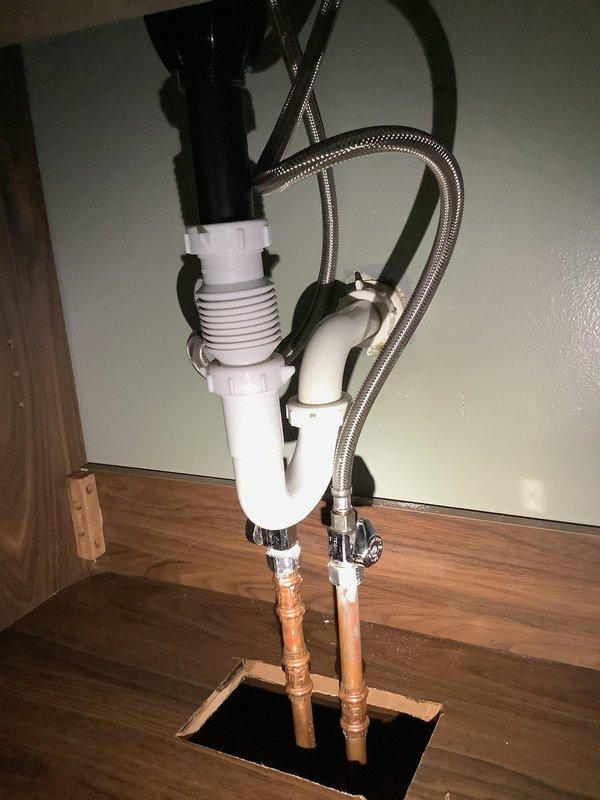 Responded to service call for water leak at first floor bathroom vanity trap following recent customer installation. Upon inspection, identified improper connection at P-trap assembly beneath newly installed vanity. Tightened slip joint connections on white PVC P-trap system and verified proper alignment of drain components. Tested system for leaks by running water through vanity drain and confirmed repair successful with no further water discharge at trap connections.