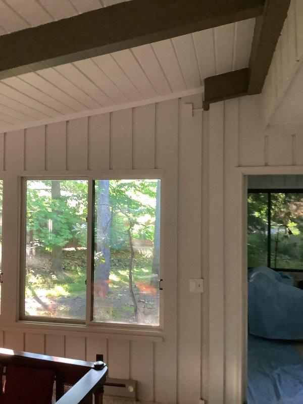Completed installation of a single-zone mini-split system in a sunroom with white paneled walls and ceiling. Mounted indoor air handler unit and connected refrigerant lines, condensate drain, and electrical connections to outdoor condenser. System tested and verified operational upon completion.