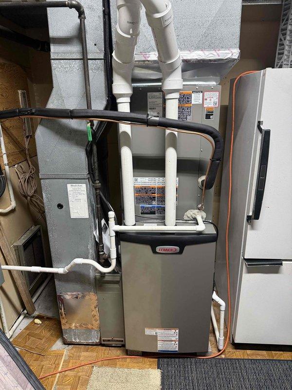 Completed full HVAC system installation including outdoor condensing units and indoor Lennox furnace. Installed three exterior AC condenser units on concrete pad against building exterior wall with proper clearances and drainage considerations. Interior installation included new Lennox furnace unit mounted in basement utility area with complete venting system using white PVC exhaust piping, copper refrigerant lines with insulation, black metal conduit for electrical connections, and dedicated electrical panel. All components properly secured to concrete block wall, system tested and verified operational.