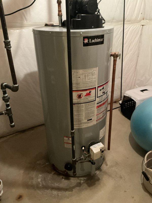 Responded to service call for leaking hot water heater. Upon arrival, found Lochinvar brand tanked water heater over 10 years old with visible water accumulation at base and moisture staining on concrete floor beneath unit. Inspected unit and determined active leak present, consistent with age-related failure of tank integrity. Documented equipment condition with photographs showing water heater installation, associated copper piping connections, gas control valve assembly, and overhead plumbing infrastructure. Advised customer of findings and recommended replacement due to age of unit and nature of leak.