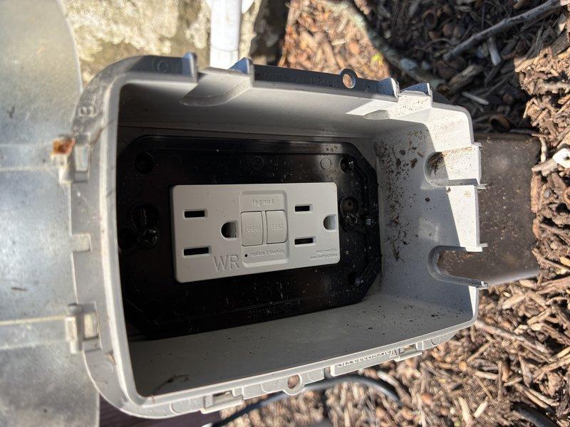 Performed diagnostic assessment of non-functioning outdoor lighting system and exterior electrical junction box. Inspection revealed potential rodent damage to exterior wiring near weatherproof GFCI outlet and concrete cylindrical structure in landscaped area. Documented conditions with photographs and provided estimate for repairs including new outdoor junction box installation and wiring replacement to restore outdoor lighting functionality.