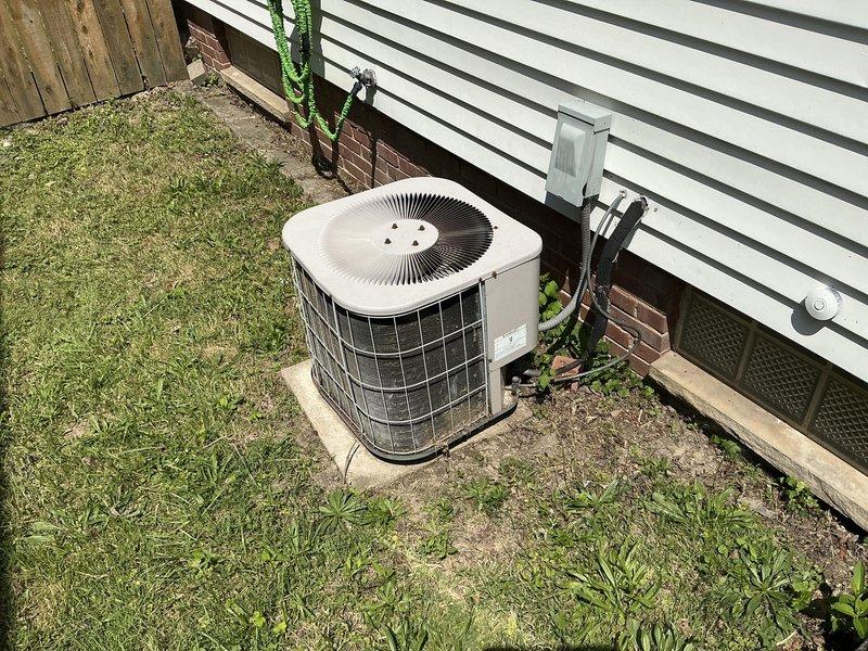 Conducted on-site evaluation of non-functional HVAC system with outdoor air conditioning unit and indoor furnace, both exceeding 20 years of service life. System was blowing warm air only, indicating compressor failure or refrigerant loss in the outdoor condensing unit. Documented existing equipment configuration including beige outdoor AC unit with cylindrical fan grille positioned on ground-level pad with electrical conduit and refrigerant lines running to building, and indoor furnace installation with air handler in basement utility area showing significant dust accumulation on components and ductwork. Provided comprehensive replacement estimate for complete HVAC system upgrade to address failed cooling capacity and aging equipment.