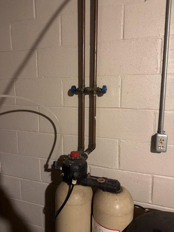 Responded to service call for non-functioning water softener system that was completely dried up with unknown age. Upon inspection, assessed three-tank water treatment configuration including dual filtration/conditioning tanks and demand-style brine tank with black control valve assembly. System showed signs of age with typical wear on copper supply lines, brass fittings, and control components. Documented existing installation conditions including electrical connections, plumbing configuration, and equipment status for customer review and future service recommendations.