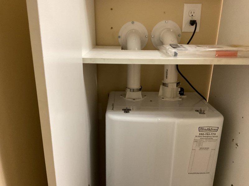 Replaced existing 2011 Navien tankless water heater with new Navien NPE 240a2 unit in cabinet installation. Reconfigured venting system by routing exhaust and intake through cabinet into attic space, terminating with concentric vent kit through roof. Abandoned existing exterior air intake and exhaust pipes in place to preserve siding integrity, sealing penetrations with spray foam insulation from interior. Installed new isolation valves on water connections and converted CPVC water piping to copper. Ran condensate drain line to hub drain connection. Installed 15 feet of new 1-inch black iron pipe for natural gas supply line with flex connector at appliance. Provided electrical outlet for unit power supply. Unit staged for LP gas conversion capability pending natural gas service availability. All components installed within tight cabinet constraints, ensuring proper clearances and access for future service.