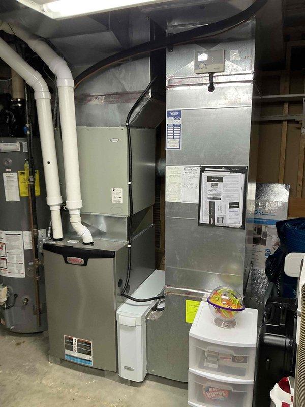 Provided estimate for complete air conditioning system replacement due to refrigerant leak in existing 13+ year old unit. Assessed outdoor cylindrical condenser unit with tower-style configuration and corresponding indoor HVAC equipment including furnace and air handler located in basement utility area. Documented existing system conditions with photographs showing equipment age, installation configuration, and leak source to support replacement recommendation rather than repair given unit age and refrigerant loss.
