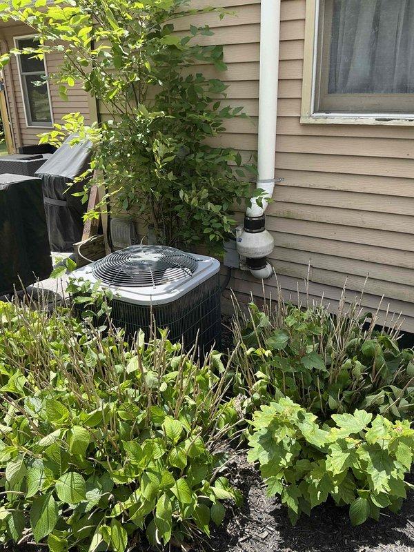 Conducted on-site assessment for residential air conditioning system replacement. Evaluated 10-year-old outdoor condensing unit experiencing refrigerant R-410A leak. Inspected exterior condenser unit located in side yard adjacent to foundation plantings, noting unit condition and accessibility for replacement. Assessed indoor air handler and ductwork system in basement utility area, documenting existing HVAC infrastructure including horizontal supply ductwork and equipment connections. Photographed current equipment configuration and installation environment to facilitate accurate replacement estimate preparation.