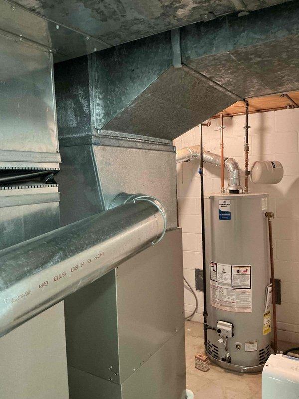 Conducted on-site assessment for residential air conditioning system replacement. Evaluated 10-year-old outdoor condensing unit experiencing refrigerant R-410A leak. Inspected exterior condenser unit located in side yard adjacent to foundation plantings, noting unit condition and accessibility for replacement. Assessed indoor air handler and ductwork system in basement utility area, documenting existing HVAC infrastructure including horizontal supply ductwork and equipment connections. Photographed current equipment configuration and installation environment to facilitate accurate replacement estimate preparation.