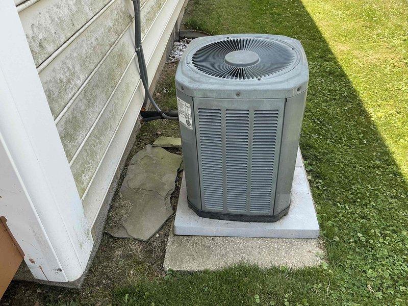 Completed estimate for replacement of 21-year-old residential air conditioning system. Evaluated existing outdoor condensing unit showing signs of age and wear, positioned on cracked concrete pad adjacent to home exterior. Assessed indoor air handler/furnace unit located in basement utility area with connected ductwork and refrigerant lines. Documented current system configuration including copper refrigerant piping, PVC condensate drainage, and galvanized supply ductwork. Provided replacement recommendations and pricing options for new AC system installation.