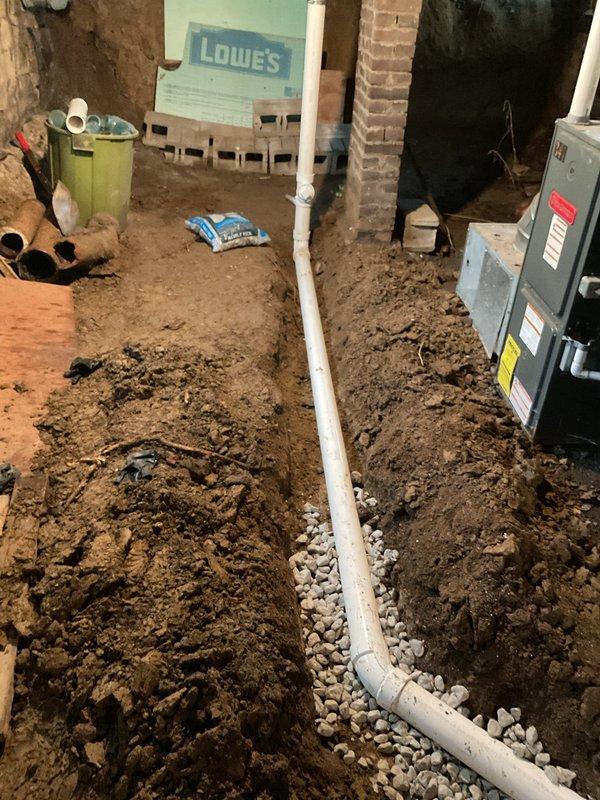 Excavated and exposed broken clay main drain line in basement dirt floor, rerouting drainage system around existing furnace to main stack. Installed new PVC piping from exposed clay section to copper main stack connection, ensuring proper pitch and alignment. Reworked kitchen drain line underground with appropriate pitch and tied into new drainage system. Hand-dug trenches to access deteriorated clay piping, installed new pipe on gravel bed, and backfilled excavated areas with original soil upon completion.