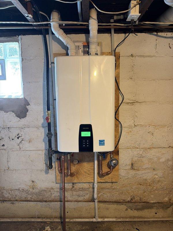 Removed existing conventional water heater and installed new Navien tankless water heater system in basement mechanical room. Mounted unit on wooden backing board attached to concrete block wall with proper clearances. Connected incoming water supply lines using copper piping and installed necessary shut-off valves. Ran PVC venting system through exterior wall with proper termination and weather sealing, utilizing dual-pipe configuration for combustion air intake and exhaust. Installed electrical outlet and wiring to power unit. Configured digital control panel settings and verified proper operation of all system components. Tested for gas leaks at all connections and confirmed adequate water flow and temperature output. All installation work performed in accordance with manufacturer specifications and local plumbing codes.