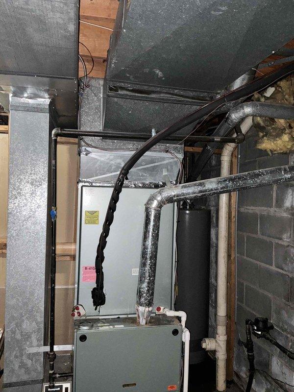 Conducted comprehensive assessment of existing HVAC system for complete replacement estimate. Evaluated outdoor condensing unit showing age-related wear with overgrown vegetation impeding proper airflow and clearance requirements. Inspected indoor air handler and ductwork system in basement mechanical space, documenting current equipment configuration and connections. Photographed both exterior and interior components to provide detailed documentation for replacement system sizing and installation planning.