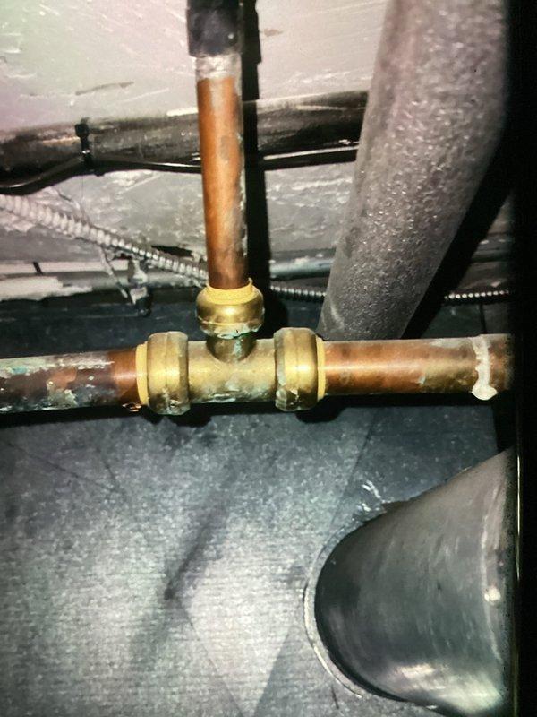 Responded to water leak in basement mechanical room caused by flue pipe installation that was routed above existing copper water line. Identified leaking T-junction with brass compression fittings on copper piping system where improper clearance during recent furnace installation created contact issue. Repositioned flue ductwork to maintain proper clearance from plumbing, repaired damaged compression fitting on water line, and verified all connections were secure with no active leaks upon completion.