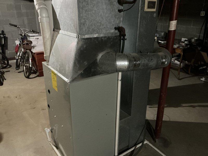 Performed comprehensive HVAC system evaluation for 47-year-old air conditioning system located in basement utility area. Assessed existing beige air handling unit with metal ductwork configuration, documented electrical panel condition showing older Stab-Lok load center with signs of age, and provided replacement estimate for complete system upgrade due to equipment age exceeding typical service life expectancy.