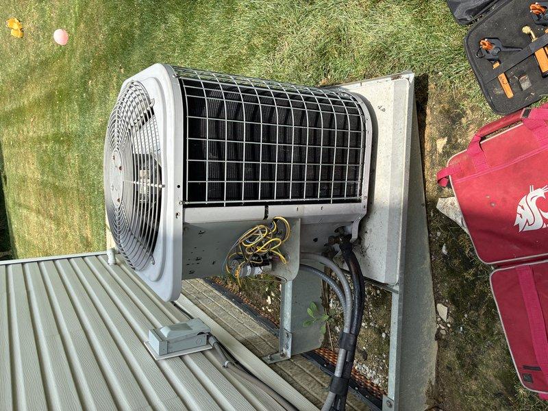 # HVAC Service Completed

Responded to service call for 15-year-old central air conditioning system failing to cool home to set temperature. Upon arrival, performed visual inspection of outdoor condensing unit and electrical components.

Accessed electrical compartment and inspected contactor, capacitor, and associated wiring connections. Photographed existing capacitor with visible manufacturer specifications and multi-colored wire terminations (yellow, blue, brown, red, and green leads). Contactor showed numbered terminals with proper wire connections intact.

Evaluated overall system condition noting age-related wear on unit housing and mounting pad. Assessed fan assembly with protective grille and condenser coil accessibility through top panel. Verified proper placement on concrete pad with adequate clearance for airflow.

Tested electrical components using standard diagnostic procedures. Checked voltage, amperage, and capacitance readings to identify failing component causing cool