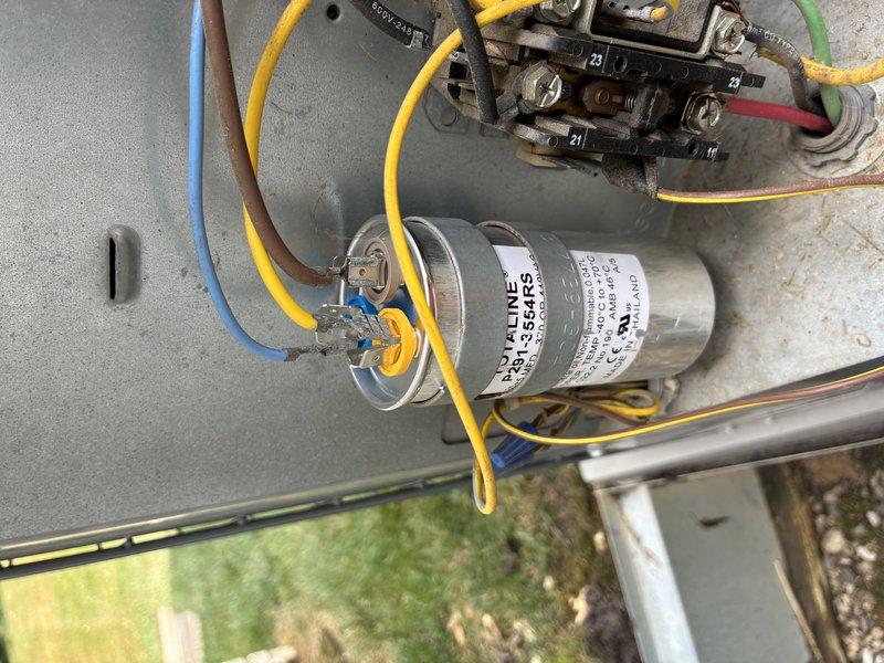 # HVAC Service Completed

Responded to service call for 15-year-old central air conditioning system failing to cool home to set temperature. Upon arrival, performed visual inspection of outdoor condensing unit and electrical components.

Accessed electrical compartment and inspected contactor, capacitor, and associated wiring connections. Photographed existing capacitor with visible manufacturer specifications and multi-colored wire terminations (yellow, blue, brown, red, and green leads). Contactor showed numbered terminals with proper wire connections intact.

Evaluated overall system condition noting age-related wear on unit housing and mounting pad. Assessed fan assembly with protective grille and condenser coil accessibility through top panel. Verified proper placement on concrete pad with adequate clearance for airflow.

Tested electrical components using standard diagnostic procedures. Checked voltage, amperage, and capacitance readings to identify failing component causing cool