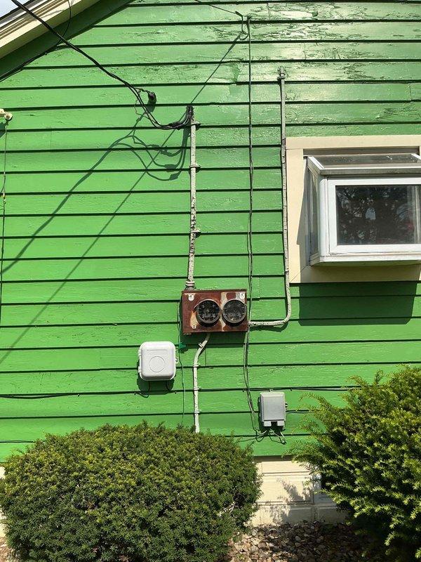 Conducted comprehensive electrical assessment of residential property following second-floor fire damage. Documented existing electrical infrastructure including exterior meter base, service entrance conductors, and interior wiring conditions. Photographed weathered exterior electrical components and interior spaces to support full house rewiring estimate for insurance and restoration purposes.
