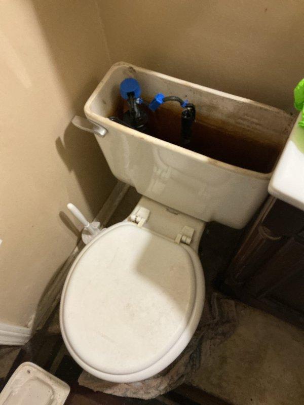 Responded to service call for toilet wax ring failure and new toilet installation request. Upon arrival, inspected existing white ceramic toilet with older-style porcelain tank showing significant interior discoloration and mineral buildup. Confirmed wax ring seal had deteriorated, causing potential leak at floor flange connection. Removed existing toilet fixture by disconnecting water supply line, unbolting from floor flange, and carefully lifting unit to prevent further water damage to dark tile flooring. Scraped old wax ring residue from floor flange and toilet base, ensuring clean mounting surface. Inspected closet flange for damage or deterioration and confirmed structural integrity for new installation. Installed new toilet fixture per customer request, positioning unit on fresh wax ring seal and securing with corrosion-resistant closet bolts. Reconnected water supply line with new flexible supply hose, verified proper alignment, and tested flush mechanism for proper operation. C
