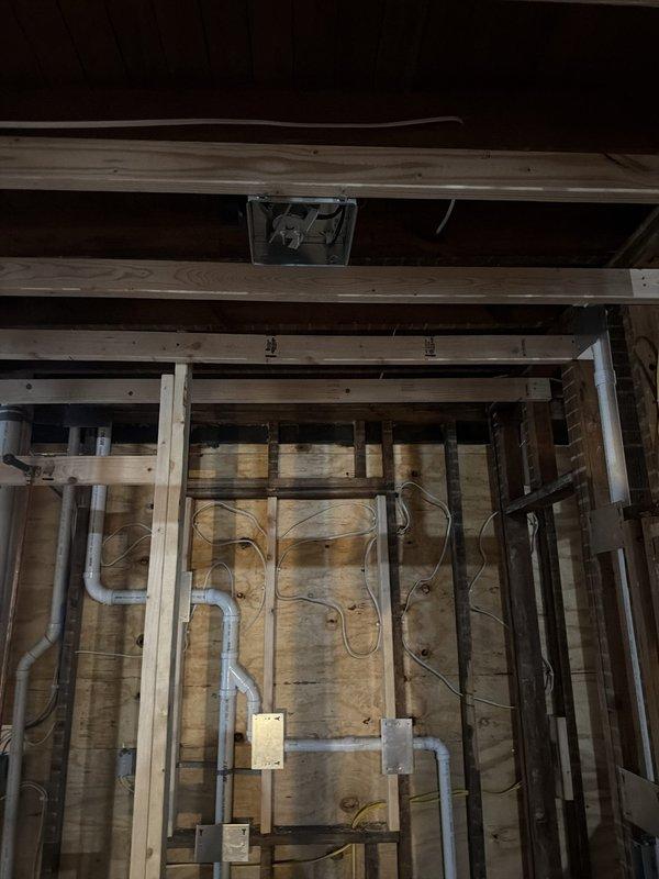 Completed comprehensive electrical rough-in and 200-amp service upgrade for residential property. Installed junction boxes, conduit runs, and wiring throughout unfinished spaces including basement and upper floor areas, with GFCI receptacle at main panel and pull-chain lighting at panel, furnace/water heater location, and three additional basement locations for temporary power. Rough-in work includes standard lighting circuits and receptacle placement per code for all rooms, kitchen 110v circuits, exterior lighting provisions near doorways, smoke detector wiring per code requirements, doorbell transformer with dual chime connections, and bathroom exhaust fan and vanity lighting circuits in framed wall cavities awaiting drywall installation.