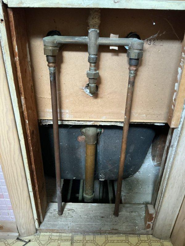 Responded to first call regarding leaking bathroom faucet. Conducted comprehensive plumbing assessment and documented existing fixture configuration. Inspection revealed exposed plumbing infrastructure including galvanized T-manifold assembly with dual valve fittings and copper supply lines running vertically through wall cavity. Examined basement water meter installation and associated copper piping system with right-angle connections on checkered tile flooring. Photographed accessible plumbing components to provide customer with detailed information on current fixture setup and potential repair options for the leaking faucet condition.