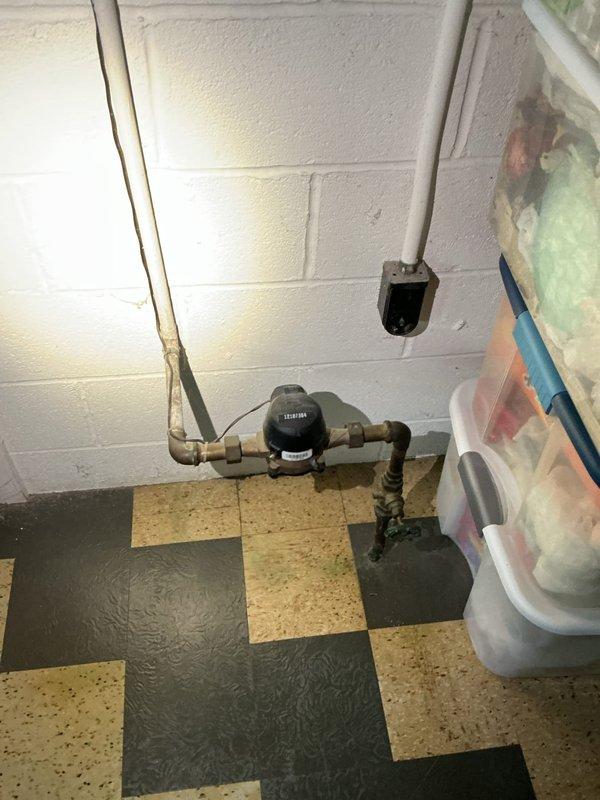 Responded to first call regarding leaking bathroom faucet. Conducted comprehensive plumbing assessment and documented existing fixture configuration. Inspection revealed exposed plumbing infrastructure including galvanized T-manifold assembly with dual valve fittings and copper supply lines running vertically through wall cavity. Examined basement water meter installation and associated copper piping system with right-angle connections on checkered tile flooring. Photographed accessible plumbing components to provide customer with detailed information on current fixture setup and potential repair options for the leaking faucet condition.