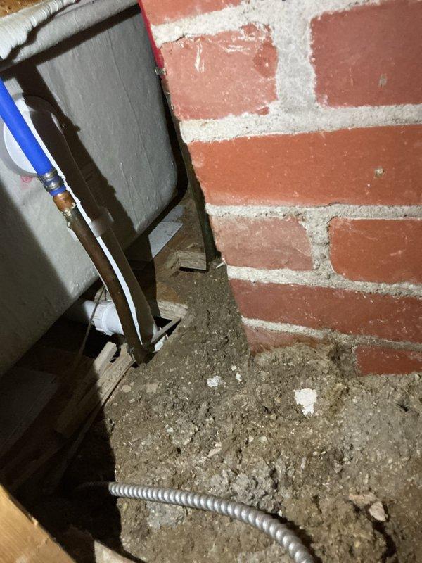 Responded to water leak complaint with visible ceiling staining below bathtub in 65-year-old residential property. Upon investigation, accessed basement utility area beneath affected bathroom to identify source of moisture intrusion. Inspected plumbing supply lines, drain assembly, and tub trap connections in crawlspace area adjacent to brick foundation wall. Documented existing conditions of exposed plumbing infrastructure and mechanical systems in basement space, including electrical conduit routing and HVAC ductwork near leak origin point. Photographed utility area showing junction of foundation wall and floor surface, as well as overhead ceiling tile conditions and metal ductwork configuration at ceiling level where moisture damage was evident. Traced leak pattern to determine whether source was from tub drain, overflow assembly, or supply line failure in aging plumbing system.