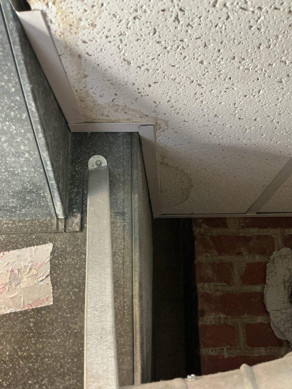 Responded to water leak complaint with visible ceiling staining below bathtub in 65-year-old residential property. Upon investigation, accessed basement utility area beneath affected bathroom to identify source of moisture intrusion. Inspected plumbing supply lines, drain assembly, and tub trap connections in crawlspace area adjacent to brick foundation wall. Documented existing conditions of exposed plumbing infrastructure and mechanical systems in basement space, including electrical conduit routing and HVAC ductwork near leak origin point. Photographed utility area showing junction of foundation wall and floor surface, as well as overhead ceiling tile conditions and metal ductwork configuration at ceiling level where moisture damage was evident. Traced leak pattern to determine whether source was from tub drain, overflow assembly, or supply line failure in aging plumbing system.