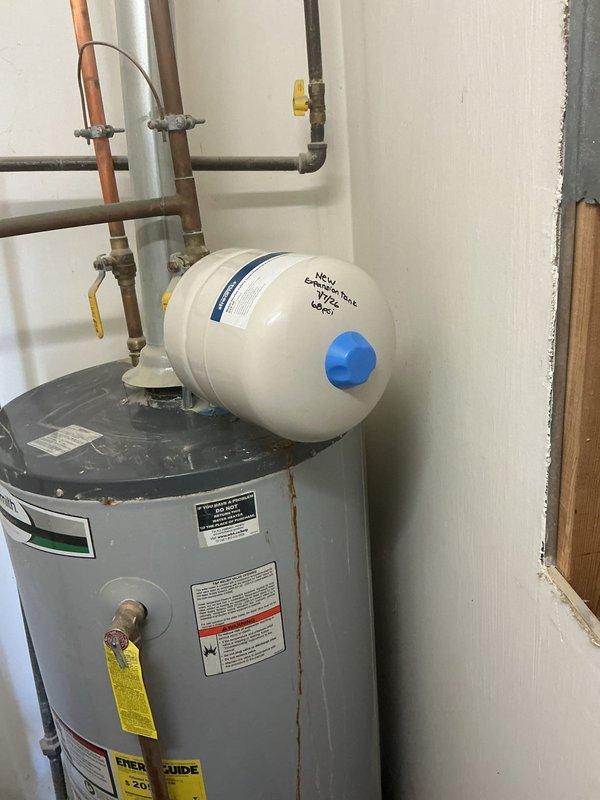 # Water Heater Expansion Tank Leak Repair

Responded to a water leak complaint involving the expansion tank mounted above the water heater. Upon inspection, confirmed active leaking from the thermal expansion tank connection point. The expansion tank exhibited significant rust-colored staining and corrosion streaking down the front surface, indicating prolonged moisture exposure from the failed connection or tank integrity compromise.

Documented the condition of the complete water heating system, including the expansion tank, copper supply piping, shut-off valves, and main water heater unit. The rust deterioration pattern originated from the upper pipe connection area where the expansion tank interfaces with the copper plumbing assembly. The corrosion and staining suggested the leak had been present for an extended period, allowing mineral deposits and oxidation to accumulate on the tank surface.

Photographed the installation showing the horizontal-mounted cream-colored expansion tan