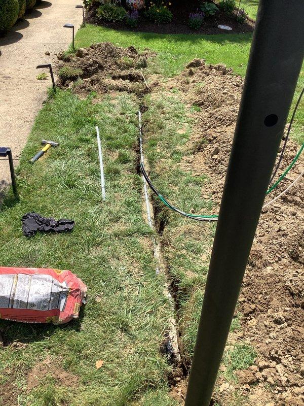 Installed wireless three-way switch system by tapping off existing garage outlet and running wiring to exterior post location. Excavated trench beneath sidewalk to route electrical conduit underground, maintaining proper depth and protection. Cut access opening in interior drywall to facilitate wire routing from switch location, then penetrated exterior brick wall to transition wiring into conduit system running to post. All wiring installed in protective conduit per code requirements, with excavated areas backfilled and compacted upon completion.